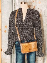 Photo of black v neck long sleeve top with small cream colored leopard print spots paired with metallic gold leather purse on a mannequin with tin background