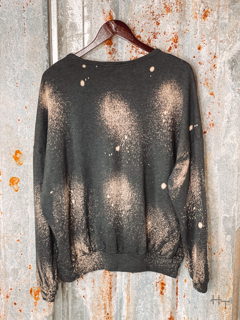 Photo of back view of charcoal sweatshirt with bleach spot details on hanger with tin background