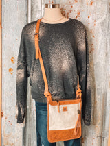 Photo of charcoal sweatshirt with bleach spot details paired with a leather and cowhide crossbody purse on a mannequin with tin background