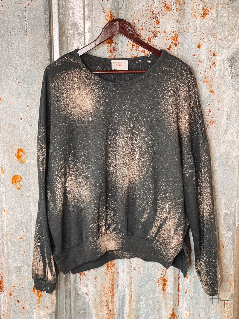Photo of front view of charcoal sweatshirt with bleach spot details on a hanger with tin background