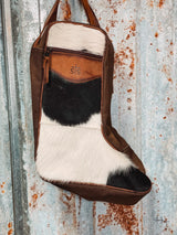 Photo of option A black and white cowhide and brown leather boot bag with front zipper pocket brown canvas sides and leather carrying handles with tin background