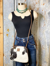 Photo of black bodysuit on mannequin with denim jeans on, accessorized with turquoise necklace and black and white cowhide purse