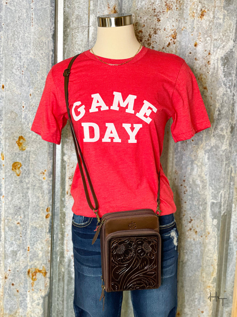 Photo of red tee shirt with words Game Day printed in white on front styled with a brown leather purse with stamped leather accents on a mannequin with a tin background