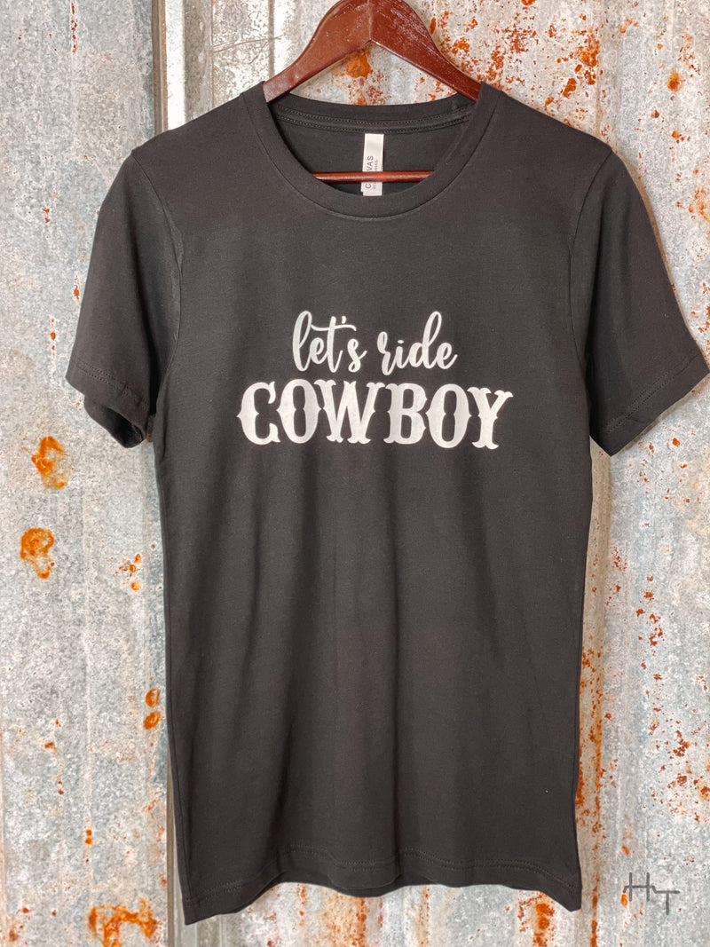 Photo of black tee shirt with Let's Ride Cowboy on front in white on a hanger with tin background