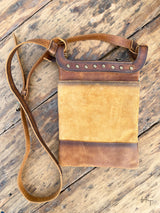Photo of back side of brown leather crossbody purse with rivet accents and long crossbody strap with wood background