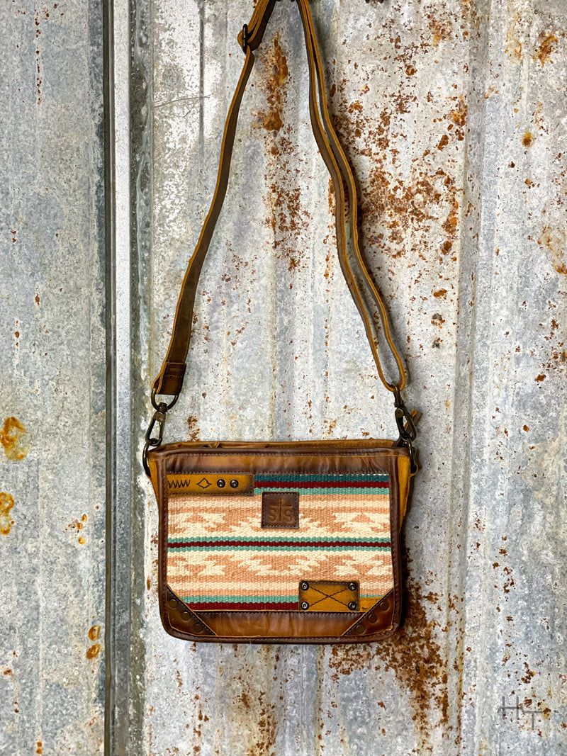 Photo of front of leather purse with pastel aztec print with sts leather patch on front and long crossbody strap with tin background
