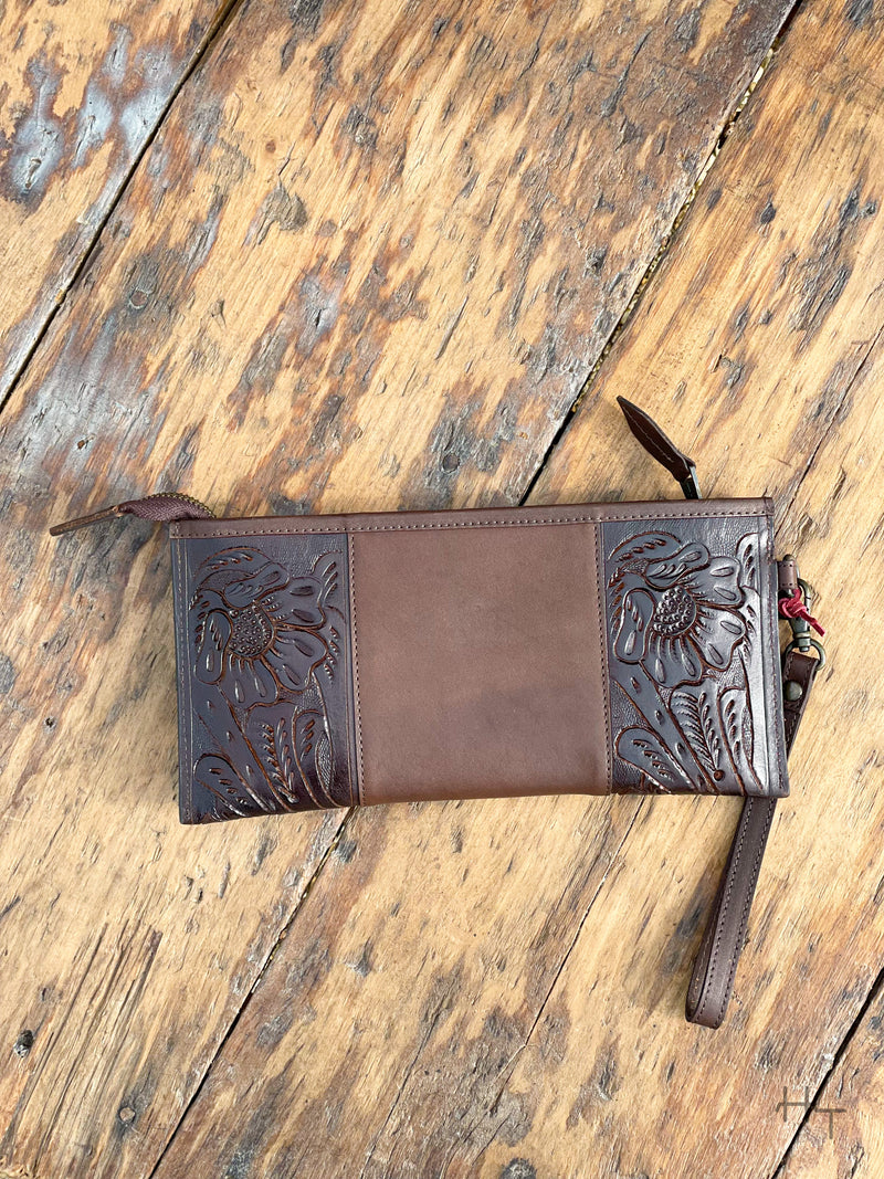 Photo of back of dark brown leather clutch wallet with tooled leather on the sides with wood back ground
