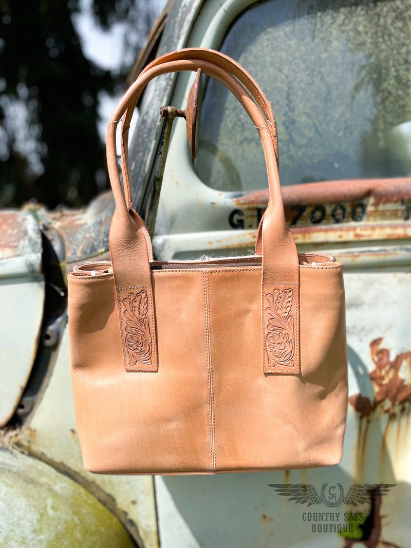 Image of back side of yipee kiyay tote purse with veggie tan leather back with 2 rolled leather shoulder straps with tooled leather detail.
